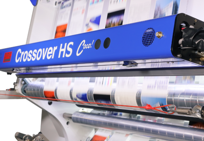 Industrial wide-format printer feeding glossy print rolls with color banners.