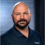 Professional headshot of a bald man with a beard wearing a navy polo shirt, neutral studio background.